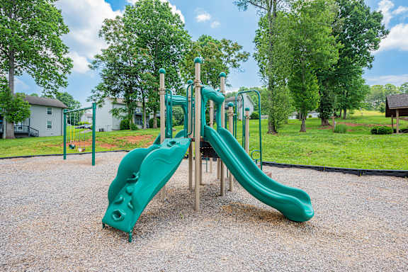 A green playground slide in the middle of a park.