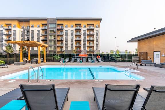 A large swimming pool with lounge chairs and a building in the background.