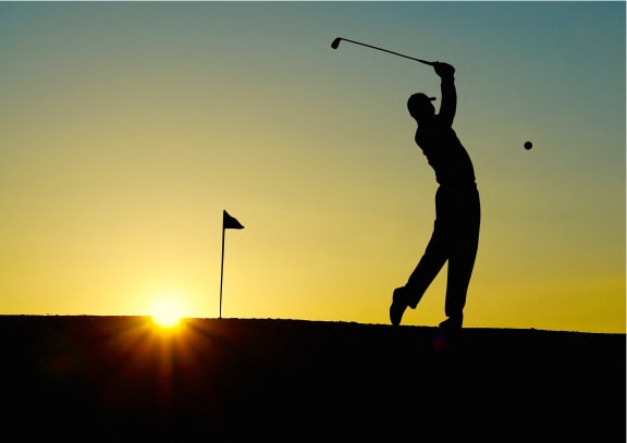 a man swinging a golf club at a ball at sunset