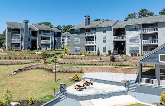 A grey apartment building with a well-maintained garden in front.