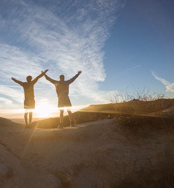 Two people standing on a hill with their arms raised in the air.