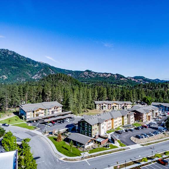 An arial view of the apartments and parking lot with the foothills of the Cascade mountains in the background at Leavenworth Haus Apartments. 