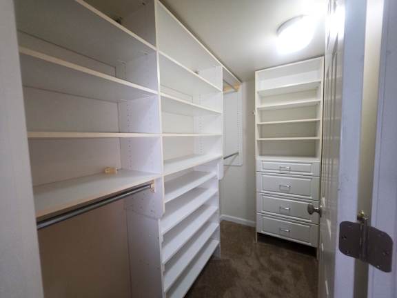 A walk in closet with white shelves and drawers.