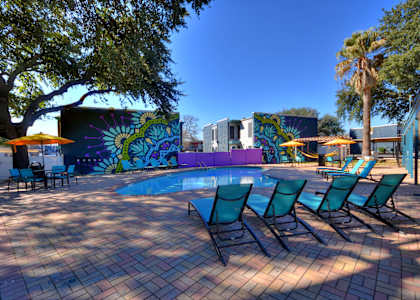 A pool surrounded by chairs and trees with a mural on the wall.
