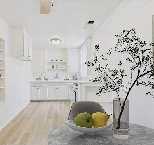 A kitchen with a table holding a bowl of fruit and a vase with a plant.