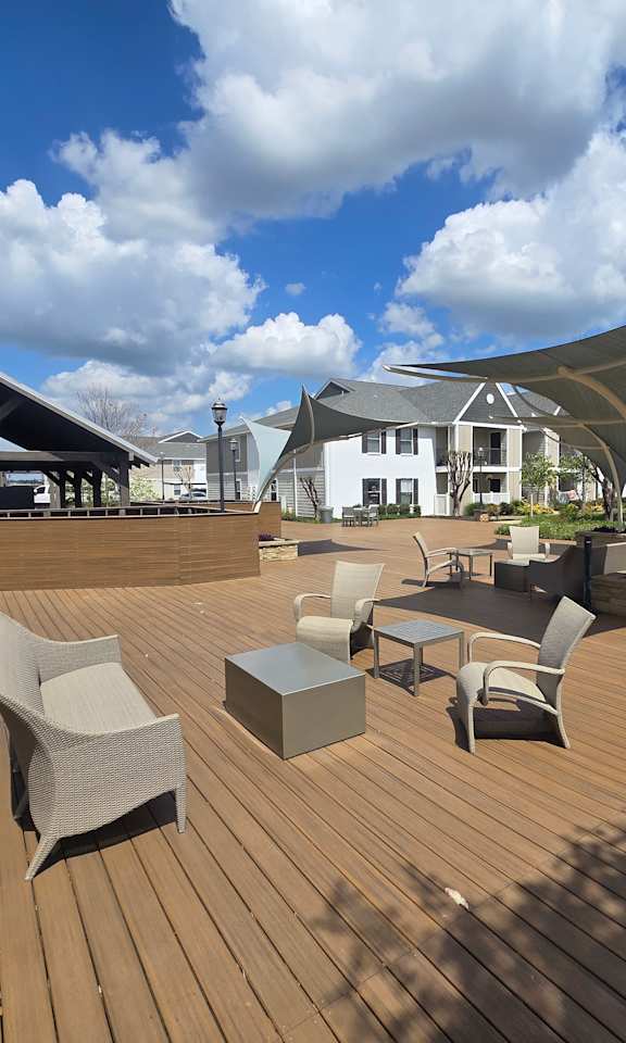 A wooden deck with chairs and tables is surrounded by buildings.
