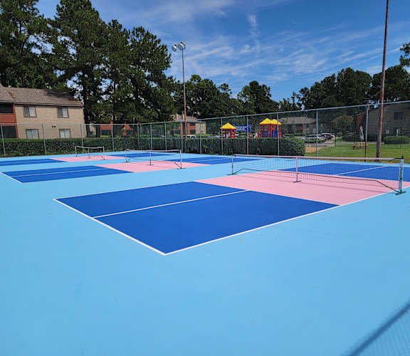 A blue and pink tennis court with a fence and trees in the background.