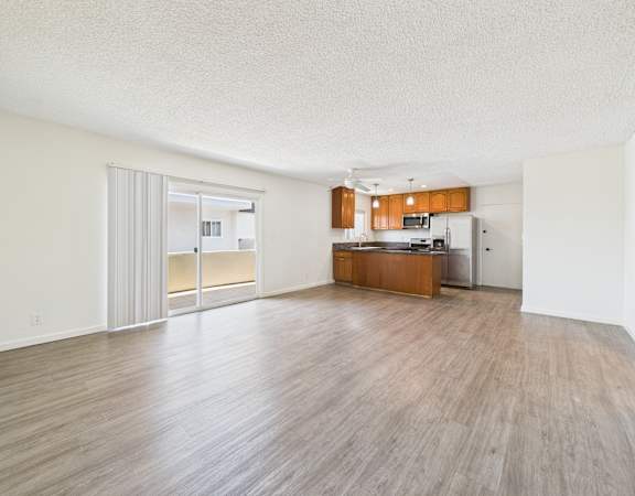 A spacious room with wooden flooring and a kitchen area in the background.