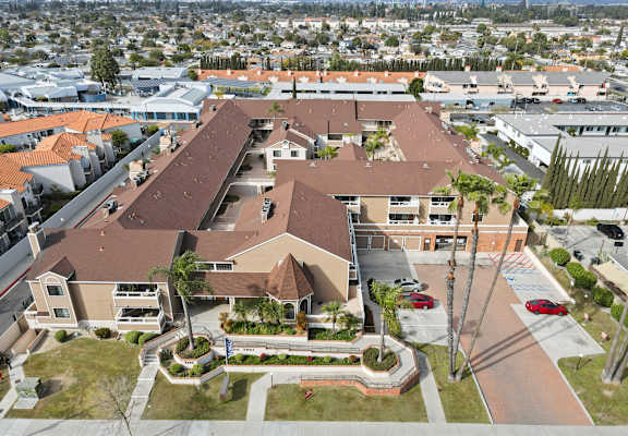 A large building with a brown roof is surrounded by a parking lot and palm trees.