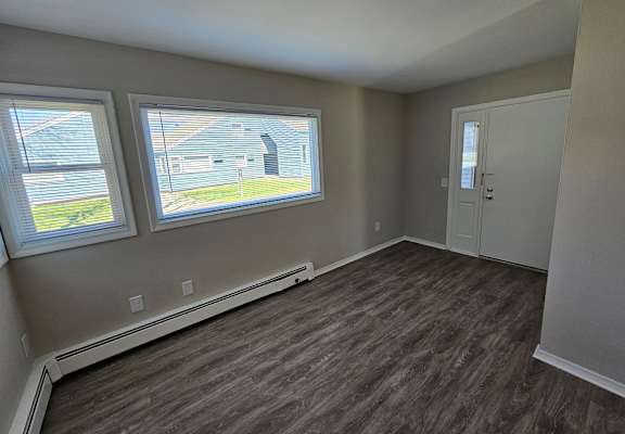 A room with brown flooring and two windows.