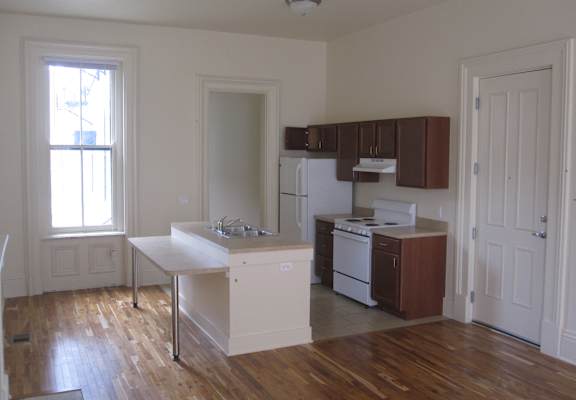 an empty kitchen with wooden floors and white appliances and cabinets
