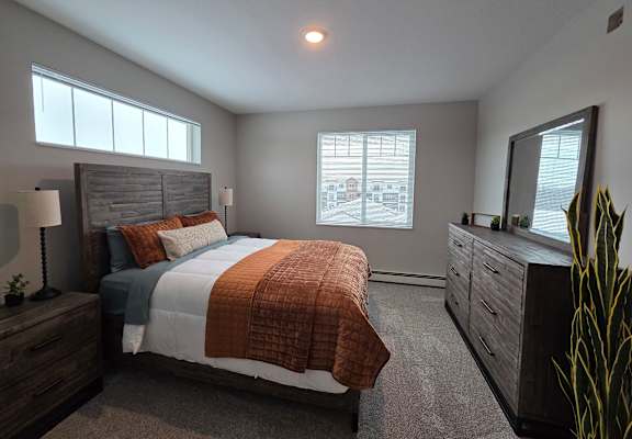 A bedroom with a large bed, a nightstand with a lamp, and a dresser with a mirror.