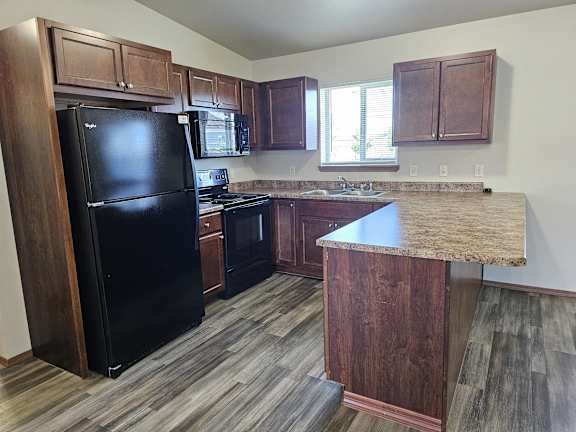 A kitchen with a black fridge and wooden cabinets.