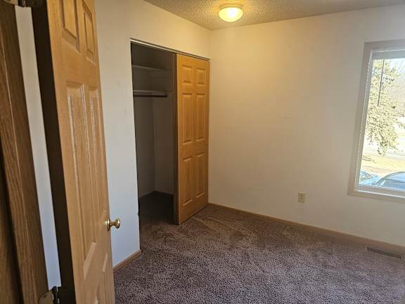 A room with a carpeted floor, a door, and a window.