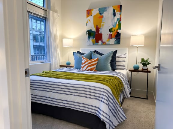 a bedroom with a bed with colorful pillows and a painting