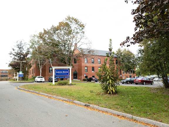 A parking lot is in front of a brick building with a sign that says "Lorimer House.".
