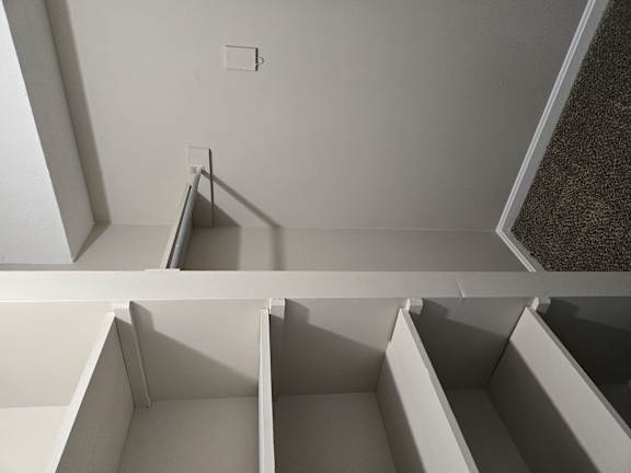 A white room with a carpeted floor and a white ceiling with a light switch.