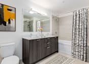 Thumbnail 7 of 21 - A bathroom with a white toilet, a sink with a mirror above it, a bathtub with a shower curtain, and a painting on the wall at One 333, Chicago, Illinois, 60605