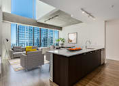 Thumbnail 6 of 21 - A modern kitchen with a large island and a living area with a couch and a chair at One 333, Chicago, 60605