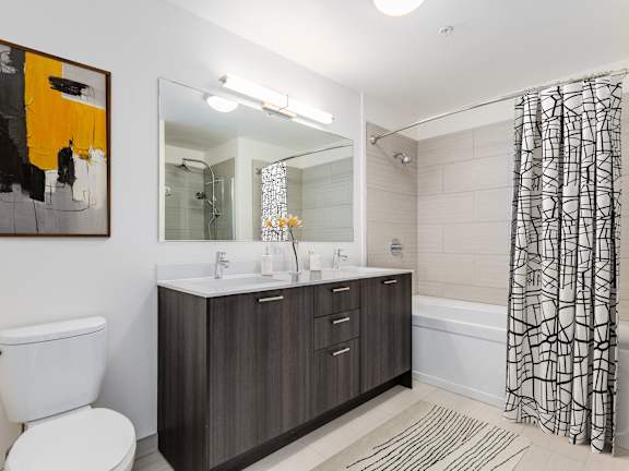 A bathroom with a white toilet, a sink with a mirror above it, a bathtub with a shower curtain, and a painting on the wall at One 333, Chicago, Illinois, 60605