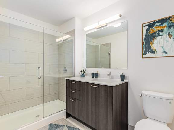 A bathroom with a white toilet, a sink with a mirror, and a glass shower stall at One 333, Chicago, 60605