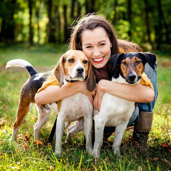 A woman is hugging two dogs in a forest.