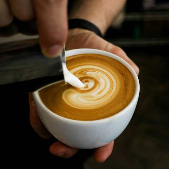A person is holding a cup of coffee with a spoon in it.