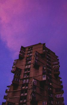 A tall brown building with many windows and balconies against a purple sky.
