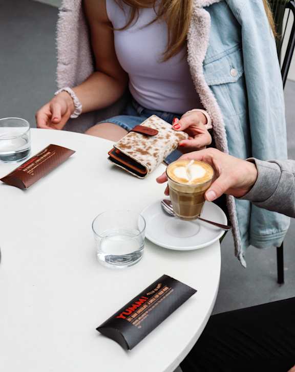 A person is sitting at a table with a cup of coffee and a chocolate bar.