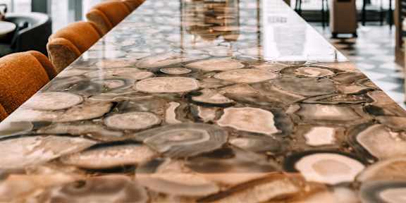 A long table with a stone pattern top is in the foreground of a bright room with a view of the city.