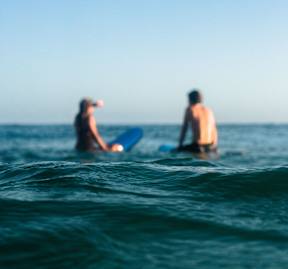 Two people are standing in the water with their surfboards.