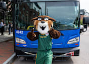 Thumbnail 4 of 10 - A person in a mascot costume stands in front of a blue bus.