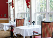Thumbnail 5 of 17 - A dining room with red chairs and white tablecloths.