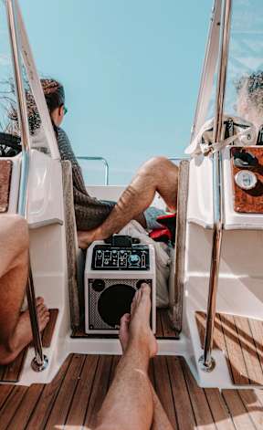 A man is sitting on a boat with his feet up, listening to music on a portable radio.