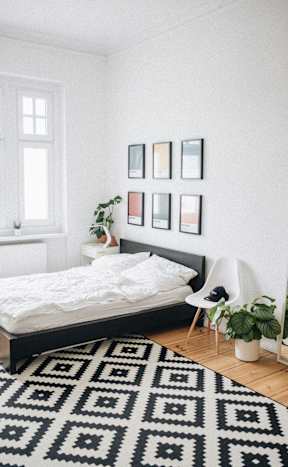 A black and white patterned rug covers the floor of a white bedroom.