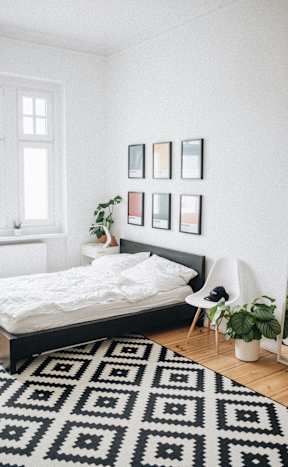 A black and white patterned rug covers the floor of a white bedroom.