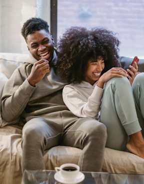 Two people sitting on a couch, one holding a phone and the other laughing.