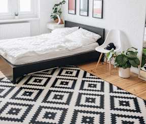 A black and white patterned rug covers the floor of a white bedroom.