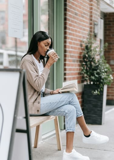 a woman sitting on a bench drinking coffee and reading a book at Ridgewood Apartments, Georgia, 30045