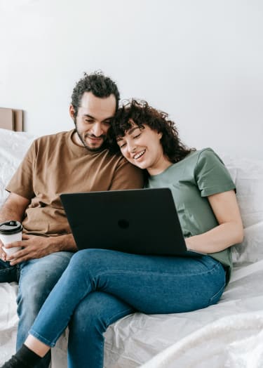 a man and woman sitting on a bed looking at a laptop computer at Ridgewood Apartments, Lawrenceville, GA