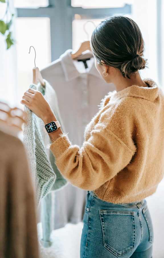 A woman in a yellow sweater and blue jeans is looking at a white shirt on a hanger.