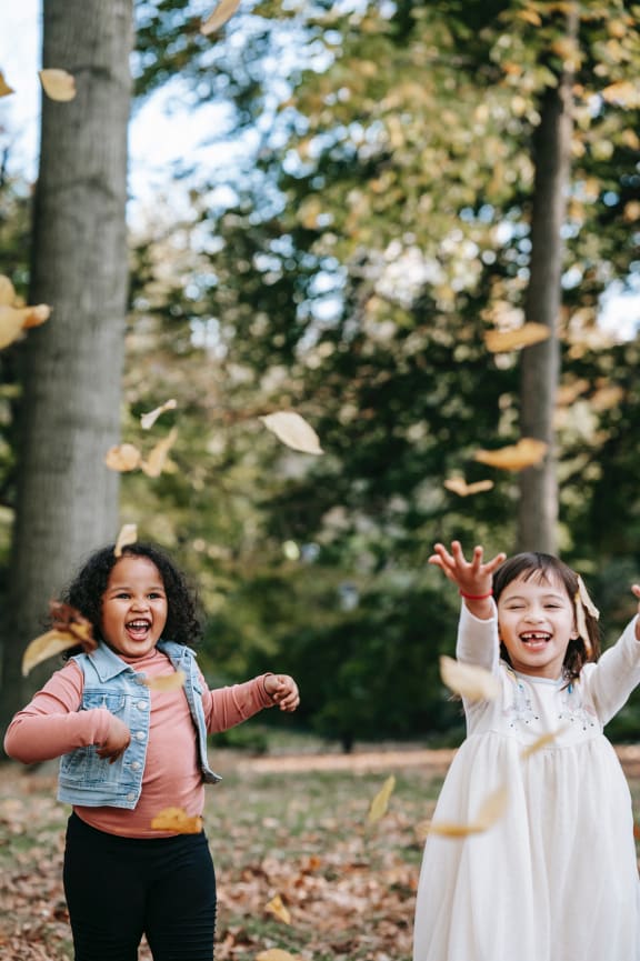 two young girls throwing leaves in the air in a park