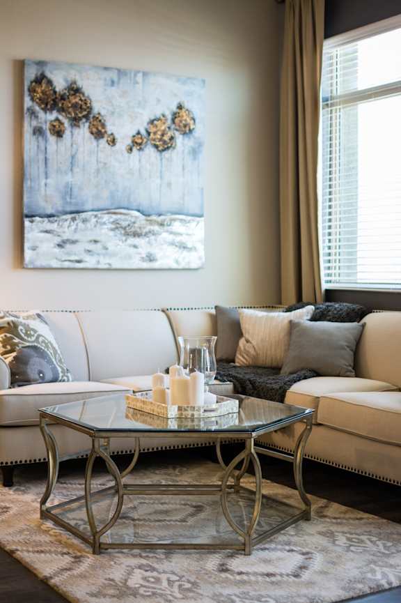 A living room with a white couch, a glass coffee table, and a painting on the wall.