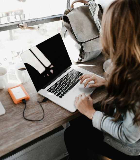 A woman is working on her laptop at a desk by a window.