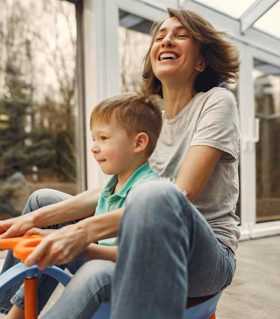A woman and a child are playing on a blue toy car together.