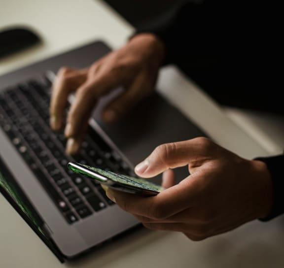 a person typing on a laptop computer while using a cell phone