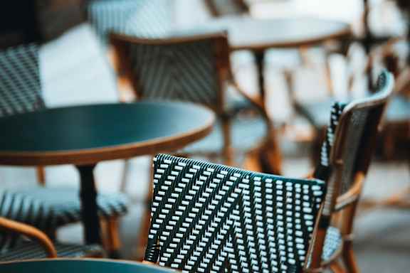 A chair with a green and white patterned seat is in the foreground of an image with tables and chairs in the background.