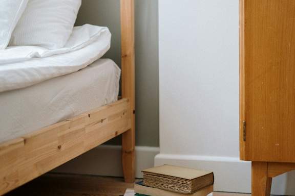 A stack of books sits on the floor next to a bed.