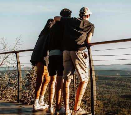 Three people standing on a balcony looking out at a view.