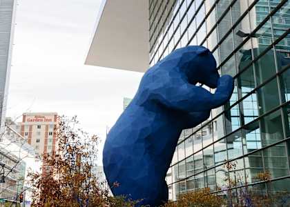 A large blue bear statue is in front of a modern glass building.